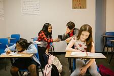 Kinder im Klassenzimmer schauen auf ein Smartphone und lachen.