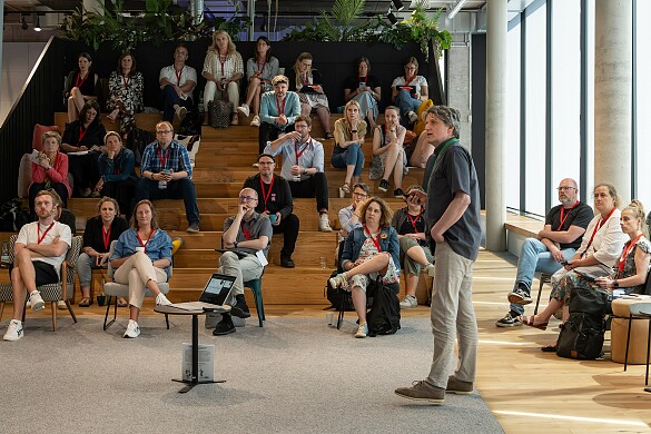 Ca. 30 Personen auf einer Tribüne hören gespannt einem Vortrag eines Referenten zu.