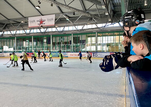 Schüler*innen schauen anderen Schüler*innen beim Eisyhockey spielen zu