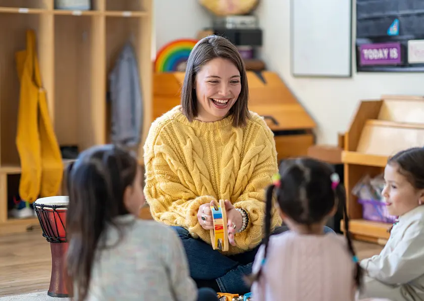 Eine Erzieherin, die mit Kindern auf dem Boden im Kreis sitzt