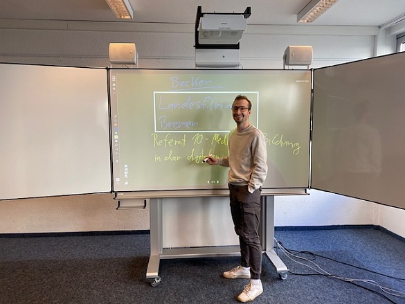 Kollege steht lächelnd an einer Interaktiven Tafel