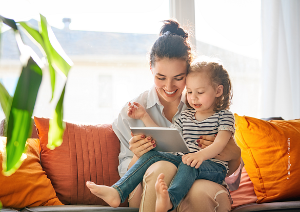 Frau mit Kind auf dem Schoß und am Tablet spielend