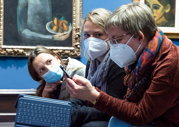 Drei Personen sitzen mit Mund-Nasen-Schutz beieinander und haben ein iPad in der Hand (Foto: Michael Schnelle)