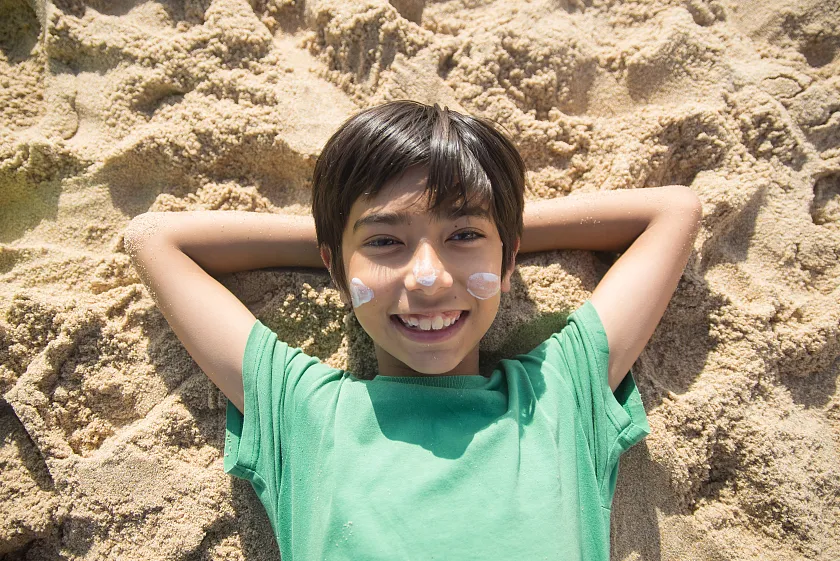 Junge, der im Sand liegt und in die Sonne schaut 