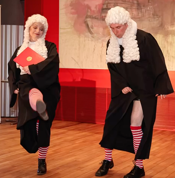 Zwei tanzende als englische Juristen mit weiße Lockenperücke verkleidete Schauspieler:innen