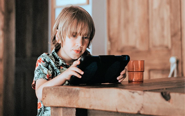 Ein Kind sitzt am Tisch mit einem Tablet