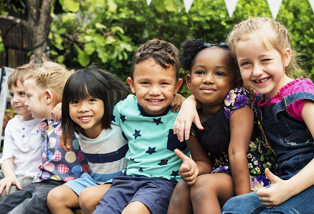 Sechs Kinder, die in einer Reihe sitzen und sich umarmen und in die Kamera lächeln