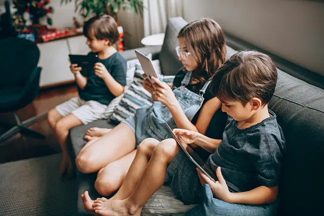 Kinder, die auf dem Sofa sitzen und in Endgeräte schauen.