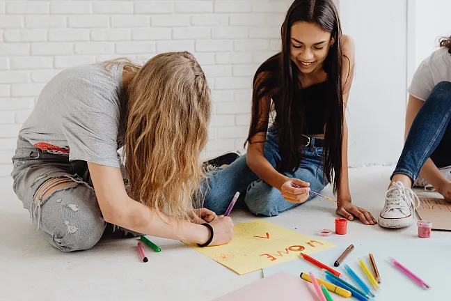 Schüler:innen, die ein Plakat malen und auf dem Boden sitzen