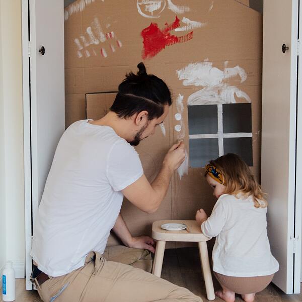 Vater bemalt ein Papp-Haus mit seiner Tochter 