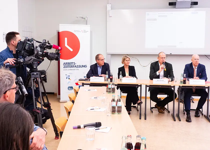 Sieben Redner:innen an einer langen Tischreihe 