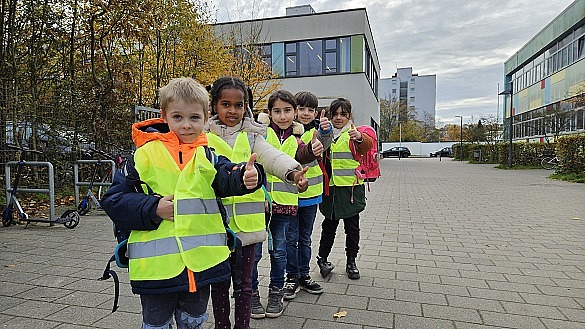 Kinder, die hintereinander in einer Reihe stehen und gelbe Warnwesten tragen