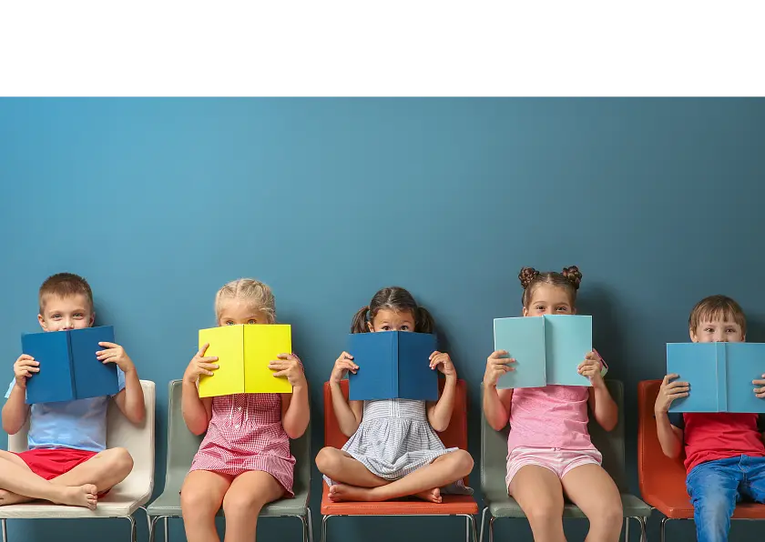 Fünf Kinder, die in einer Reihe sitzen und sich Bücher vor das Gesicht halten