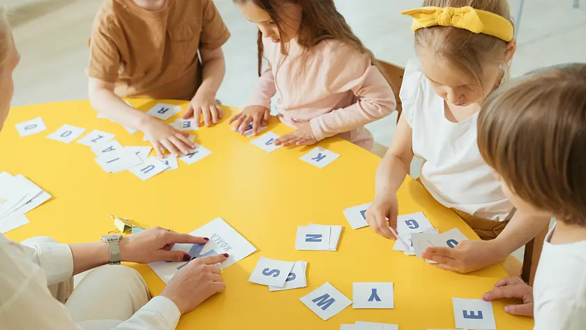 Kinder, die an einem Tisch sitzen und Buchstaben hin und herschieben