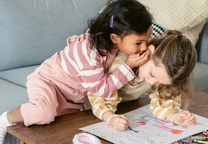 Zwei kleine Kinder, die sich etwas ins Ohr flüstern