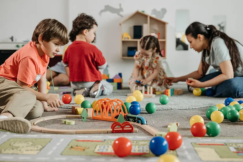 Kinder, die mir ihrer Erzieherin auf dem Boden spielen